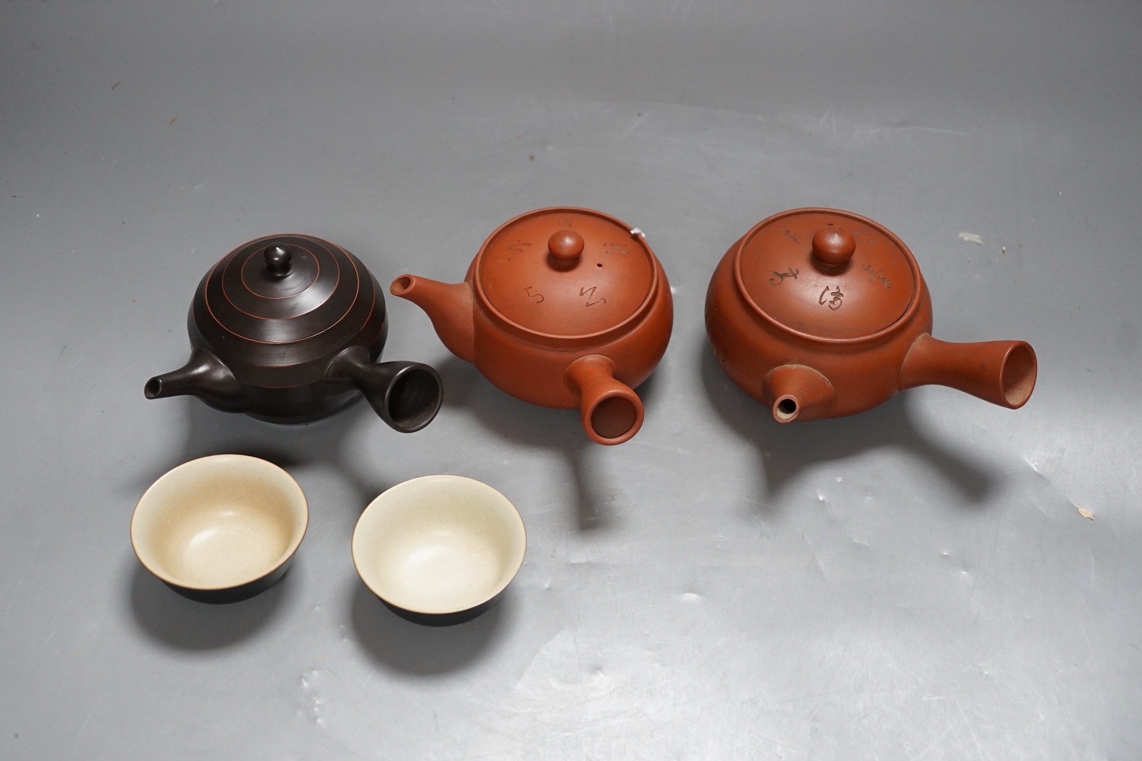 Two Japanese redware teapots, a similar brown stoneware teapot and two cups